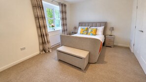 A bedroom with a bed, bedside tables, a bench, a window with curtains, and a radiator.