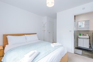 A bedroom with a bed, a nightstand, a bedside table, a bathroom with a sink, mirror, and shower.