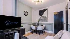 Uma sala moderna com televisão de tela plana, uma mesa de jantar com cadeiras, um relógio e uma porta.
