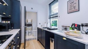 Uma cozinha moderna com armários pretos, bancada branca e uma janela com persianas.