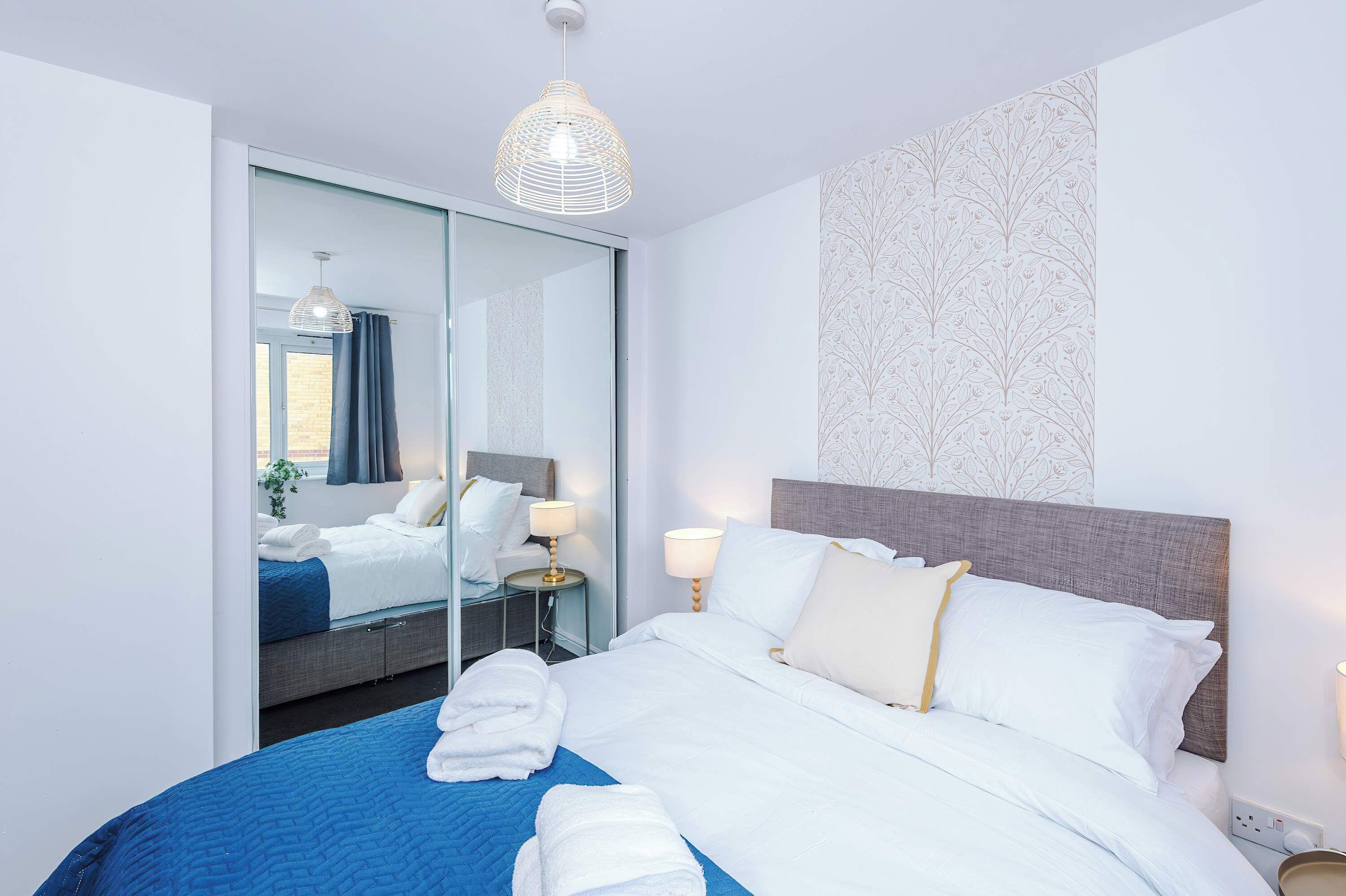 A hotel room with a bed, bedside lamps, a mirror, and a view of the outside.
