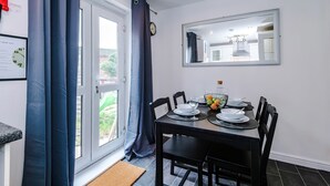 A dining area with a table set for four, a mirror on the wall, and a window with curtains. - Sleeps 5 Near Manchester Centre Free Parking (Greater Manchester)