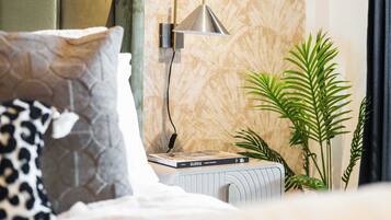 Ein ordentlich eingerichtetes Schlafzimmer mit einem Bett, Kissen, einem Nachttisch mit Büchern, einer Wandlampe und einer Zimmerpflanze.