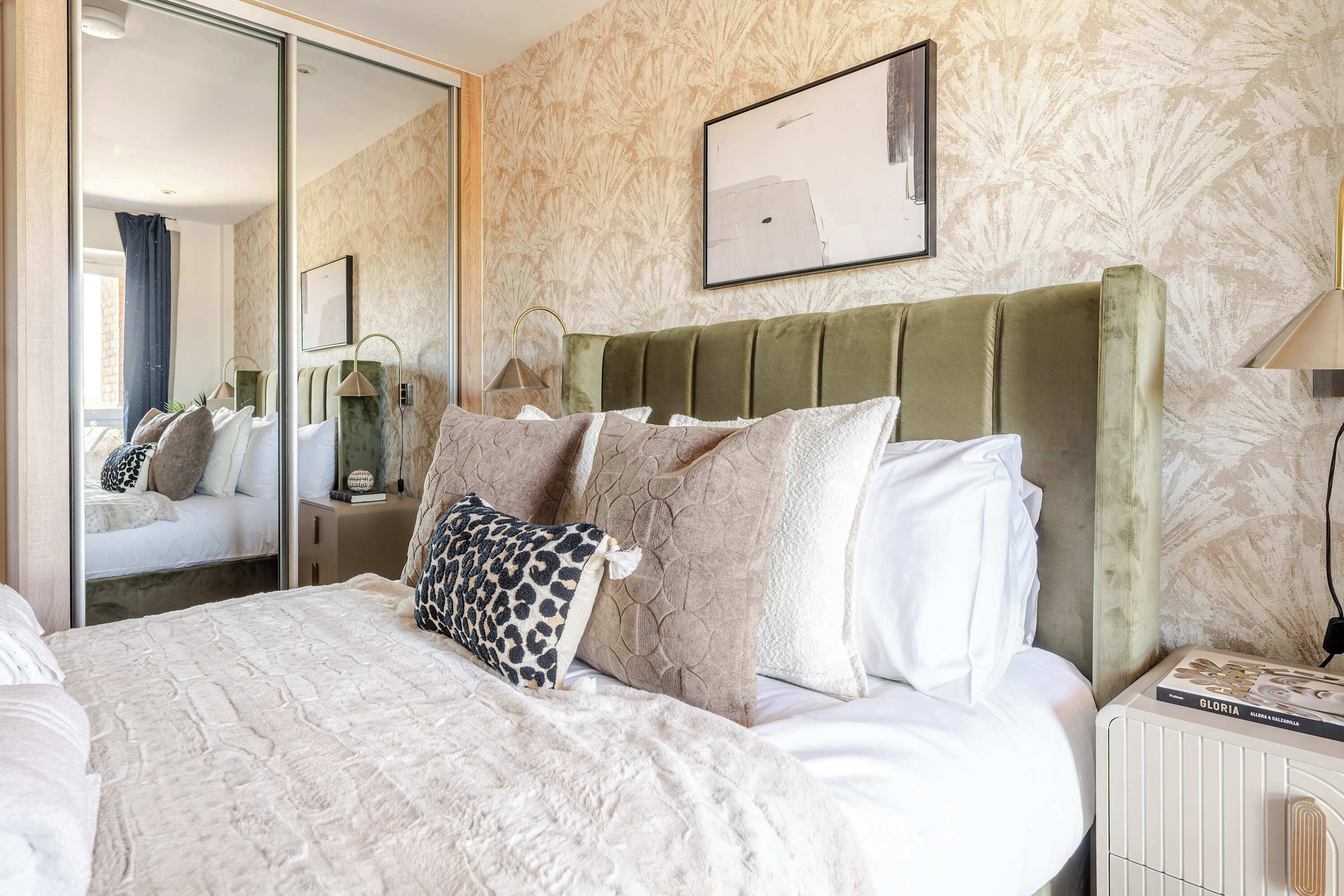 A hotel room with a bed, a mirror, a nightstand, and a wall-mounted picture.