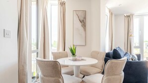 Un salón moderno con una mesa redonda blanca, sillas color beige, un sofá azul oscuro y una planta verde.