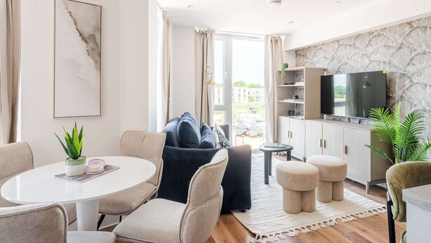 Una sala de estar moderna con una mesa redonda, sofás, otomanas, un televisor y vistas al exterior.