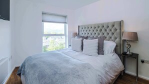 Ein Schlafzimmer mit einem großen Bett, einem Fenster, einer Nachttischlampe und Blick ins Freie.