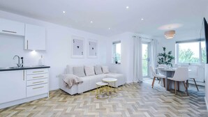 Eine moderne Küche mit weißen Schränken, ein Essbereich mit rundem Tisch und Stühlen, eine Sitzecke und ein Fischgrätparkettboden.