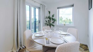 Ein Essbereich mit einem runden Tisch für vier Personen, Stühlen, einem Topf mit Pflanze und Blick ins Freie.