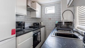 Cocina compacta con alacenas blancas, encimera negra, horno empotrado, pileta y ventana sobre la pileta.