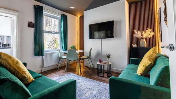 Una sala de estar moderna con sofás verdes, un comedor, un televisor de pantalla plana y un ventanal con cortinas.