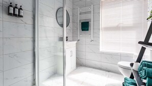 Un baño moderno con cabina de ducha de vidrio, inodoro blanco y toallero con toallas.