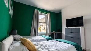 Un dormitorio con dos camas, televisión, cómoda y ventana con cortinas.