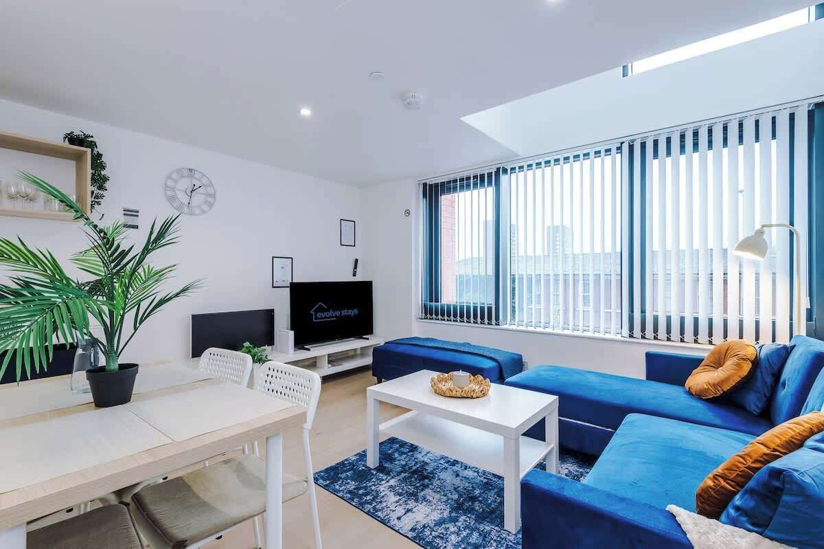 Ein modernes Wohnzimmer mit einer Couch, einem Fernseher, einem Esstisch und einem großen Fenster mit Jalousien.
