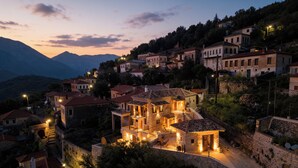 A hillside village with stone buildings, a prominent house with a balcony, and a mountain backdrop.
