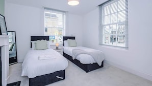 Hotellihuone, jossa on kaksi sänkyä, kattovalaisin ja suuret ikkunat.