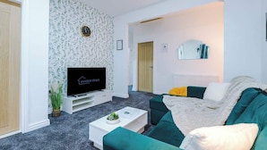 Ein modernes Wohnzimmer mit Flachbildfernseher, einer Couch, einem Couchtisch und einer Wand mit Muster.
