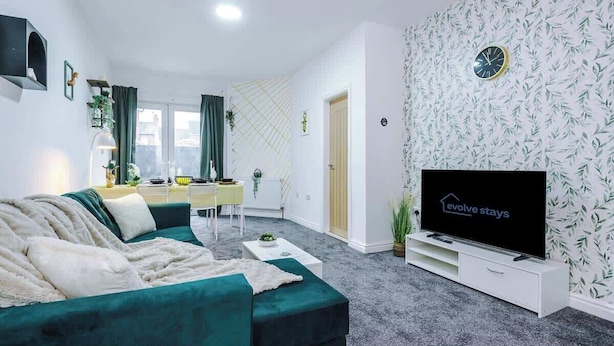 Ein Wohnzimmer mit Sofa, Fernseher, Esstisch mit Stühlen und einer Wand mit Muster.