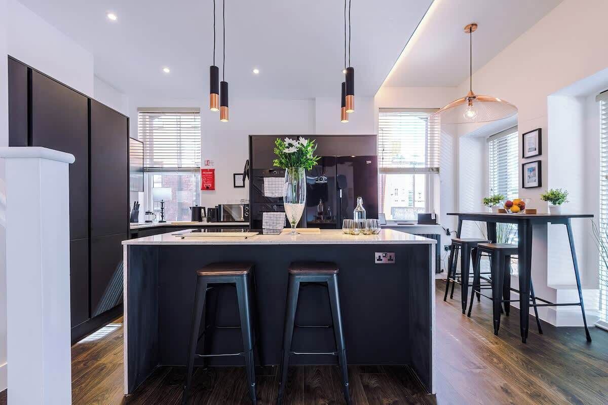 A modern kitchen with a central island, bar stools, pendant lighting, and a view of the city.