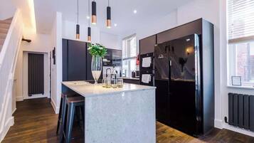 A modern kitchen with a central island, pendant lighting, and a black refrigerator.