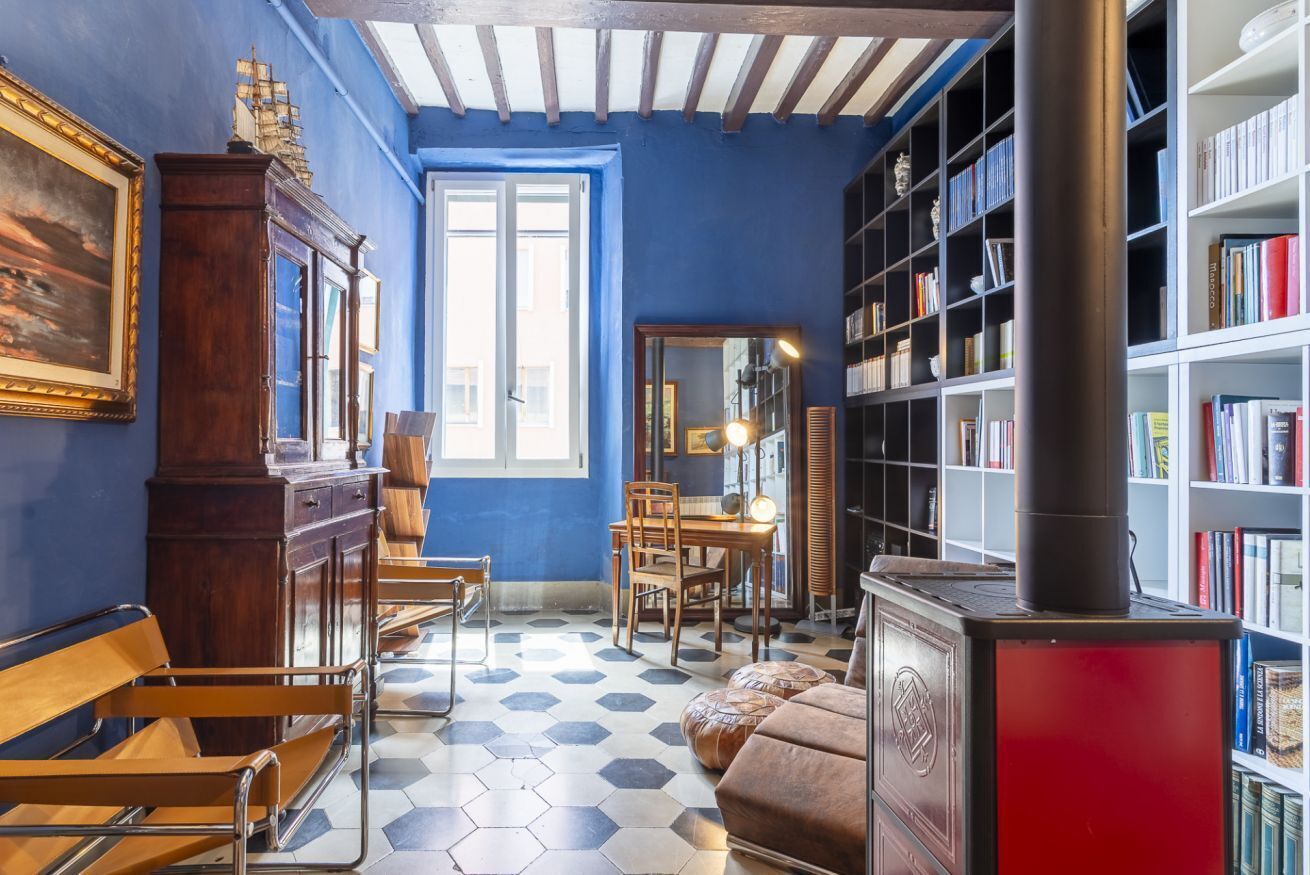 A room with a hexagonal tiled floor, a wooden bench, a table with chairs, a bookshelf, and a red stove.