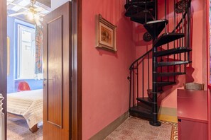 A room with a bed, a red wall, a black spiral staircase, and a door leading to another room. - GuestHost - Stylish Apartment in the Heart of Livorno (Livorno)