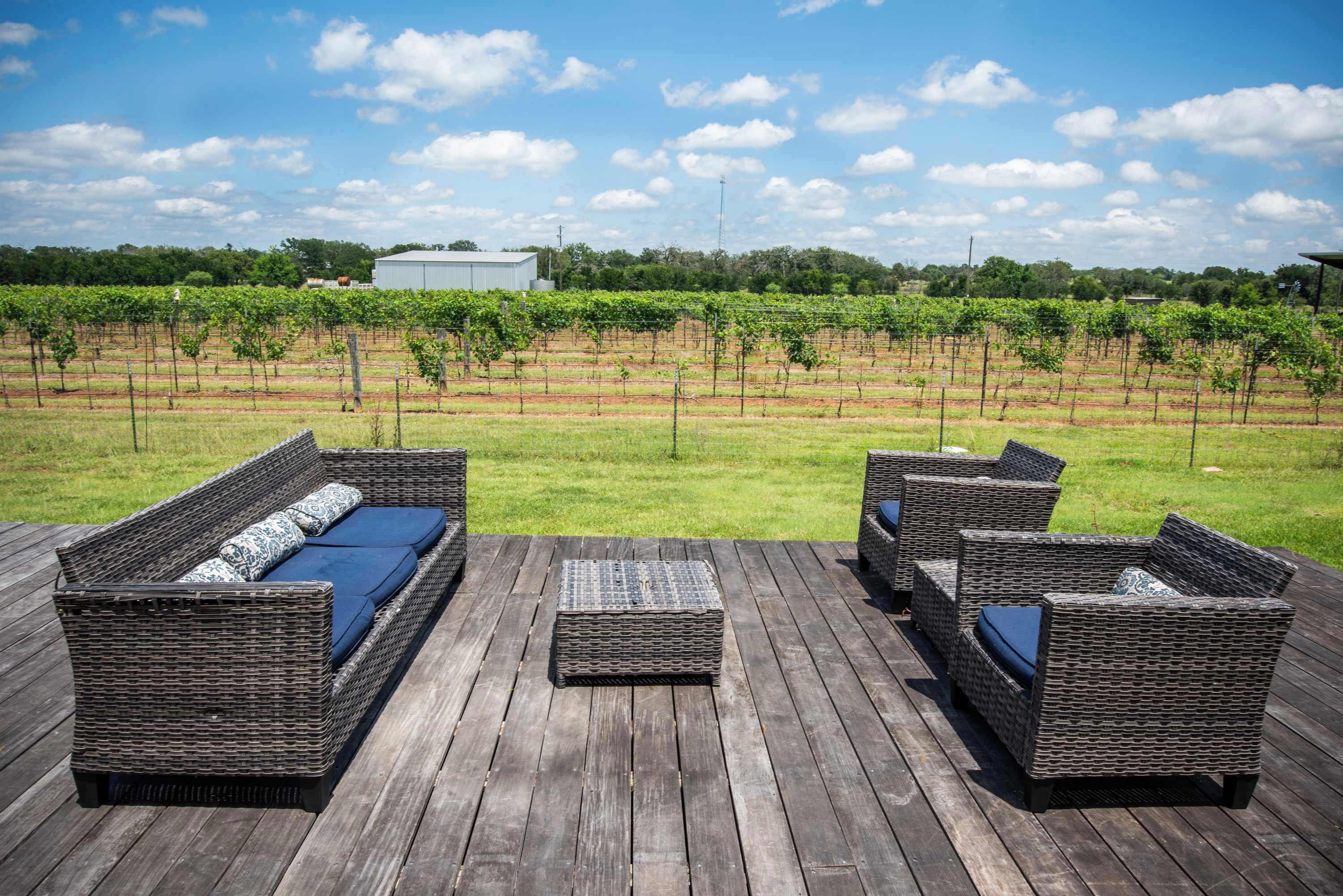 A wooden deck with wicker furniture and a vineyard view.