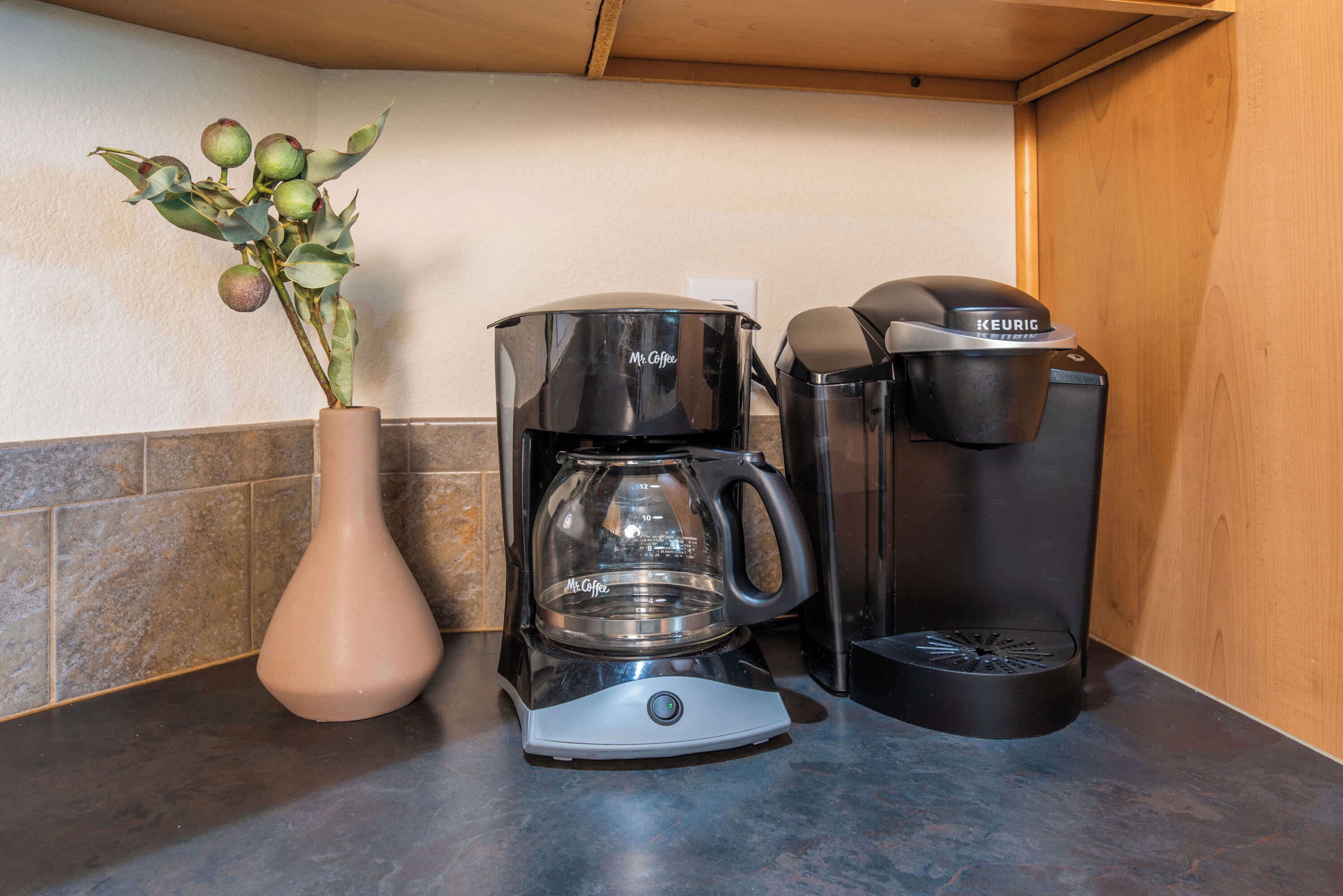Une machine à café, un appareil Keurig et un vase avec des feuilles vertes sur un plan de travail de cuisine.