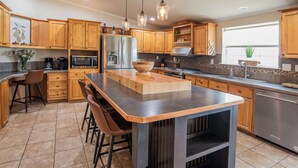Una cocina moderna con armarios de madera, una isla central, taburetes de bar y electrodomésticos de acero inoxidable.