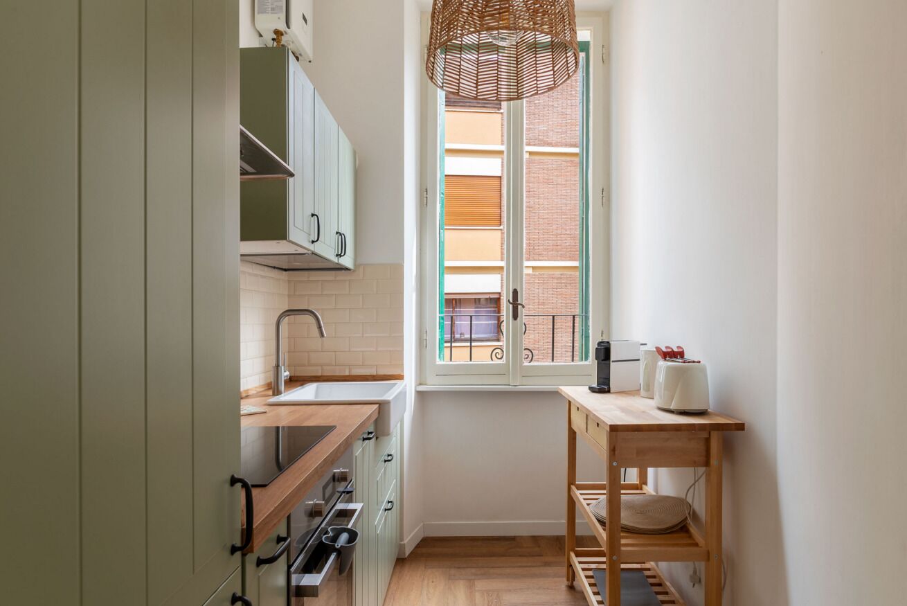 A compact kitchen with a window, a hanging light fixture, and a small dining table.