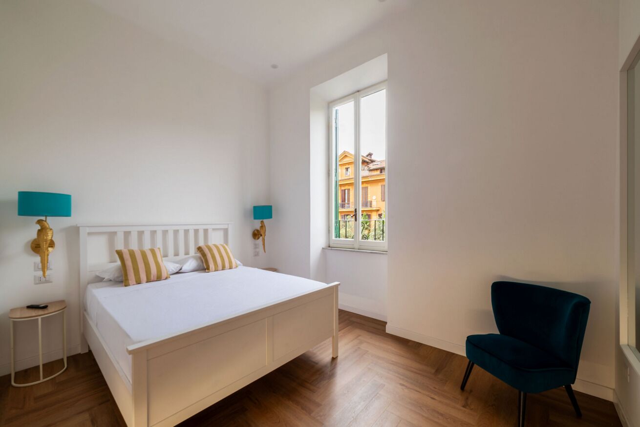 Une chambre à coucher avec un lit, une chaise, une fenêtre et une vue sur des immeubles.