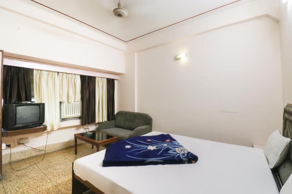 A hotel room with a bed, a chair, a television, and a window with curtains.