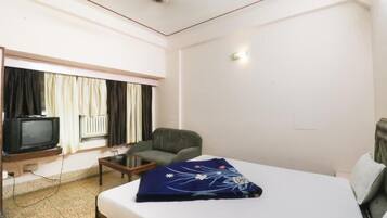 A hotel room with a bed, a chair, a television, and a window with curtains.