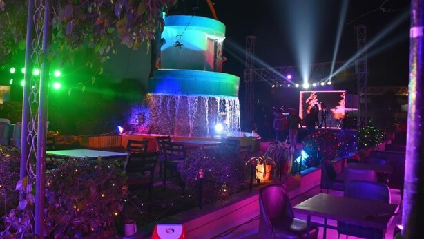 A multi-tiered fountain with water cascading down, surrounded by outdoor seating and illuminated by colorful lights.