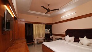 A hotel room with a bed, a desk, a chair, a television, and a ceiling fan.