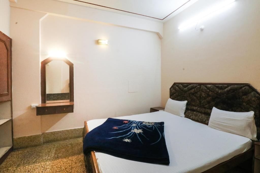 Habitación de hotel con cama, mesita de noche, espejo y lámpara de pared.