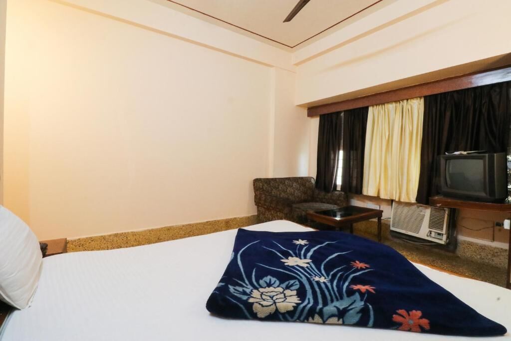 Een hotelkamer met een bed, een televisie, een stoel en een airconditioning.