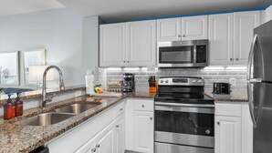 A modern kitchen with white cabinets, stainless steel appliances, granite countertops, and a coffee maker. - Majestic View Oceanfront (Panama City Beach)
