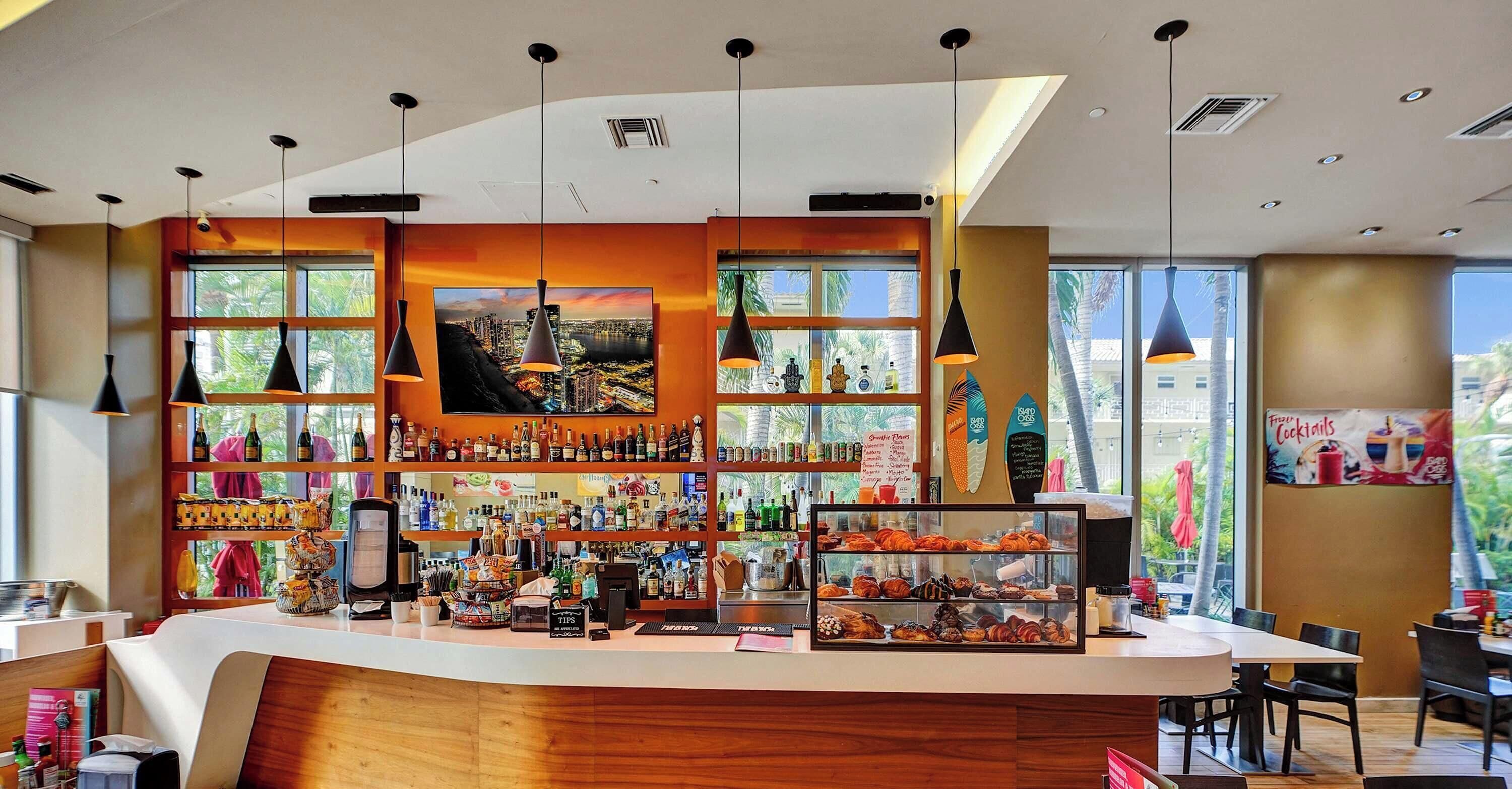 Un área de bar moderna con una barra curva, estantes con varias botellas y una vitrina con pasteles.