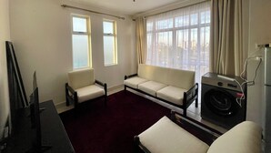 Een kamer met een bank, twee stoelen, een televisie en een wasmachine.