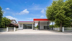 Eine Tankstelle mit rotem Vordach, weißem Zaun und blauem Himmel.