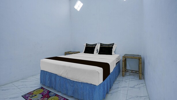 Ein Schlafzimmer mit einem Bett, zwei Kissen, einem Nachttisch, einem kleinen Hocker und einem Teppich mit Blumenmuster.