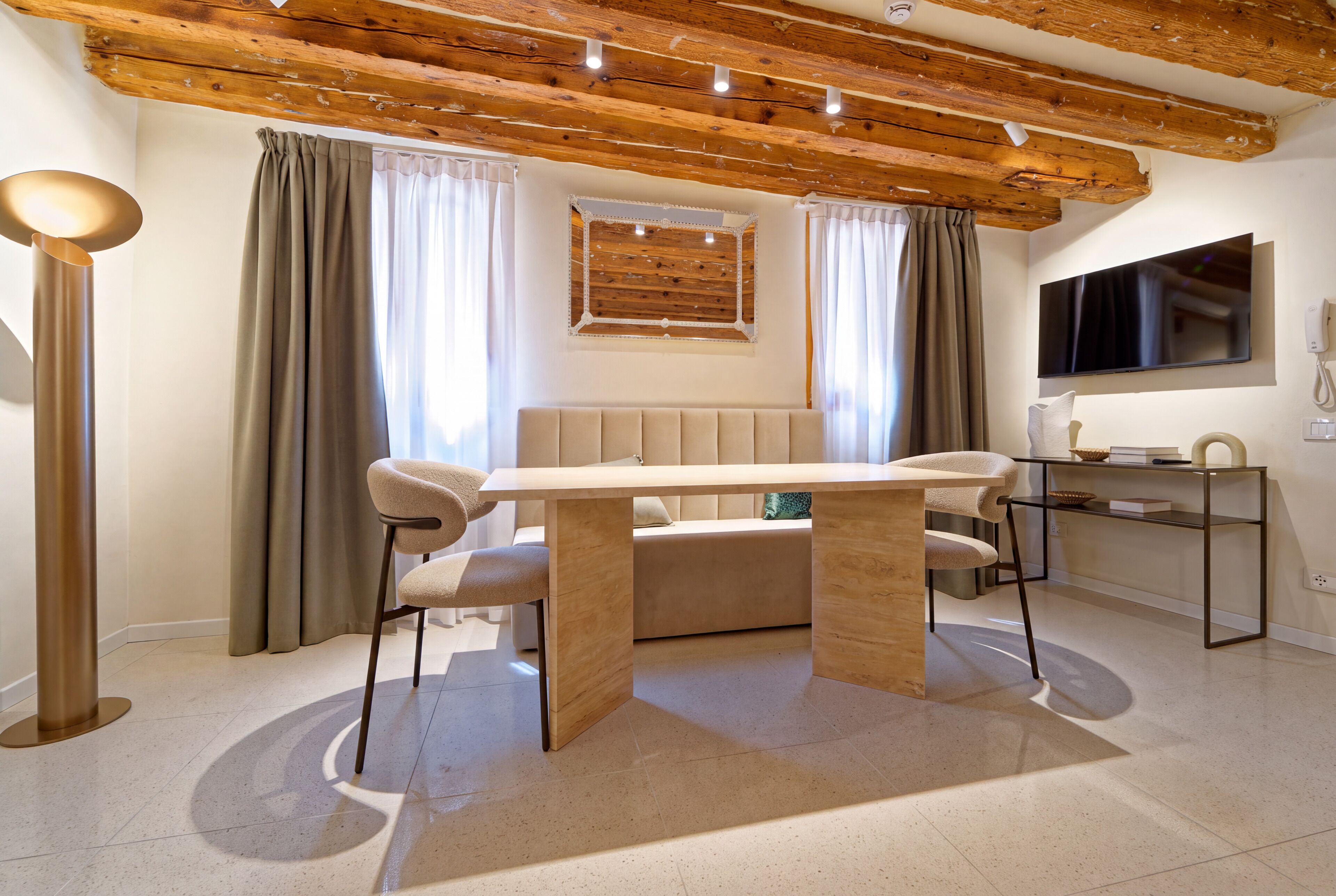 Un soggiorno moderno con soffitto in legno, un divano beige, un tavolo da pranzo e un televisore montato a parete.