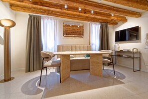 A modern living room with a wooden ceiling, a beige sofa, a dining table, and a TV mounted on the wall. - Be Mate Santa Croce (Venezia)