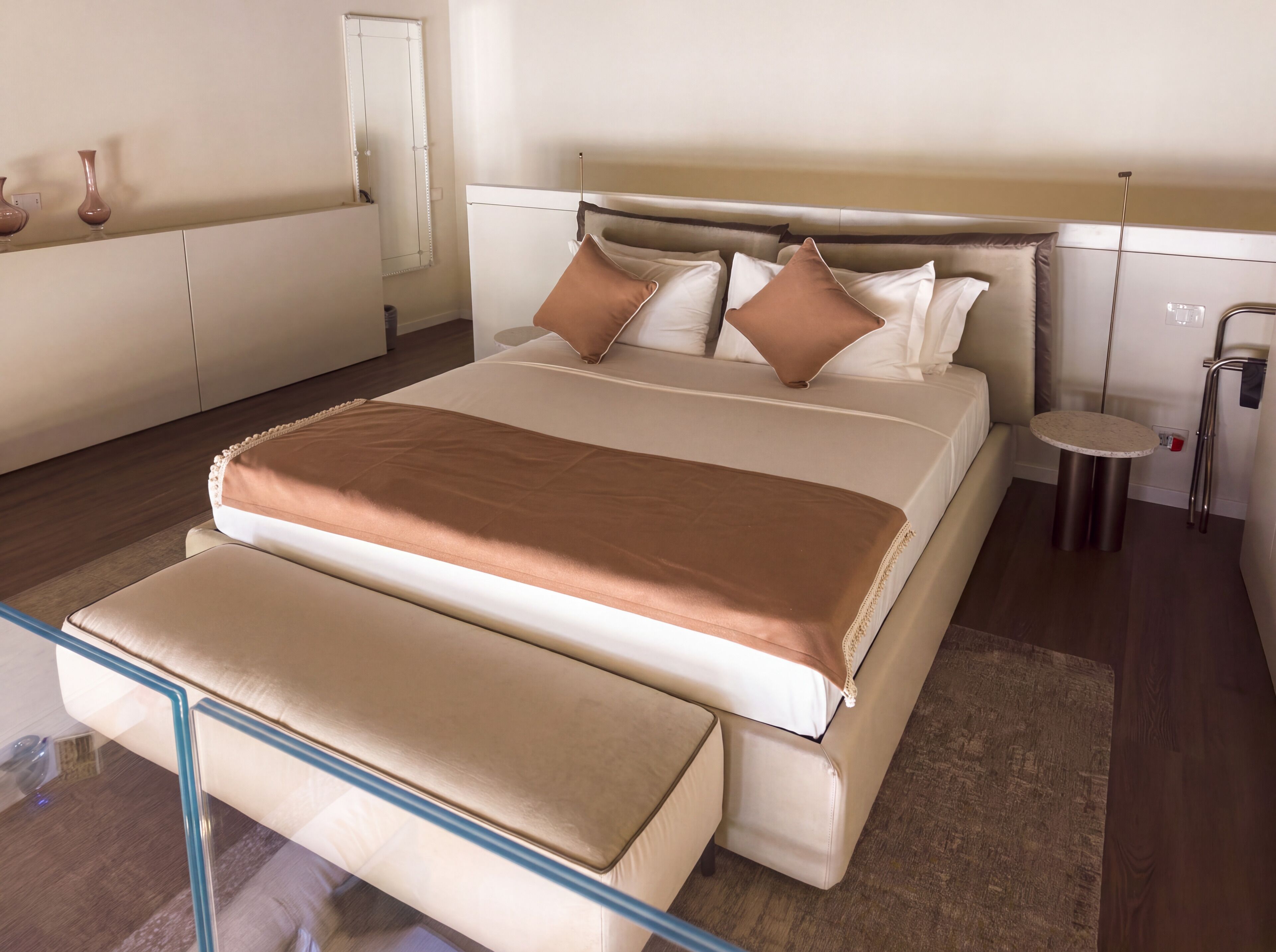 Une chambre d’hôtel moderne avec un grand lit, des tables de chevet, une table ronde et un miroir.