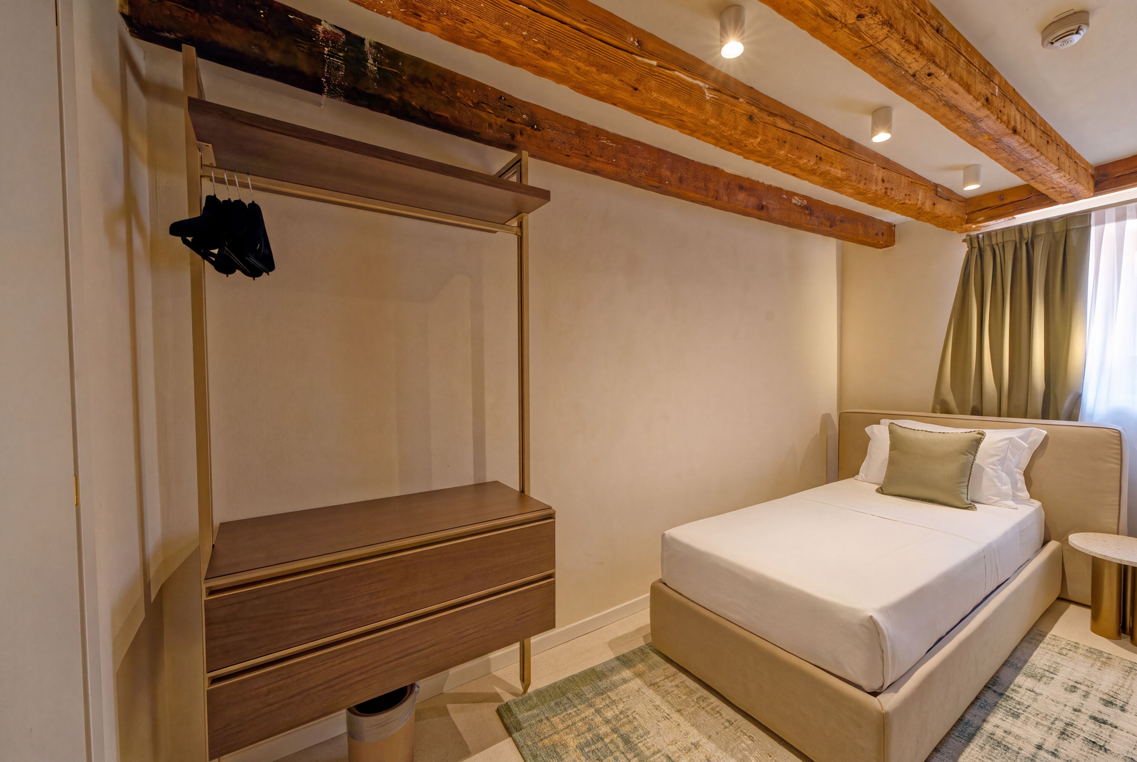 A bedroom with a bed, a wooden wardrobe, a small table, and a window with curtains.