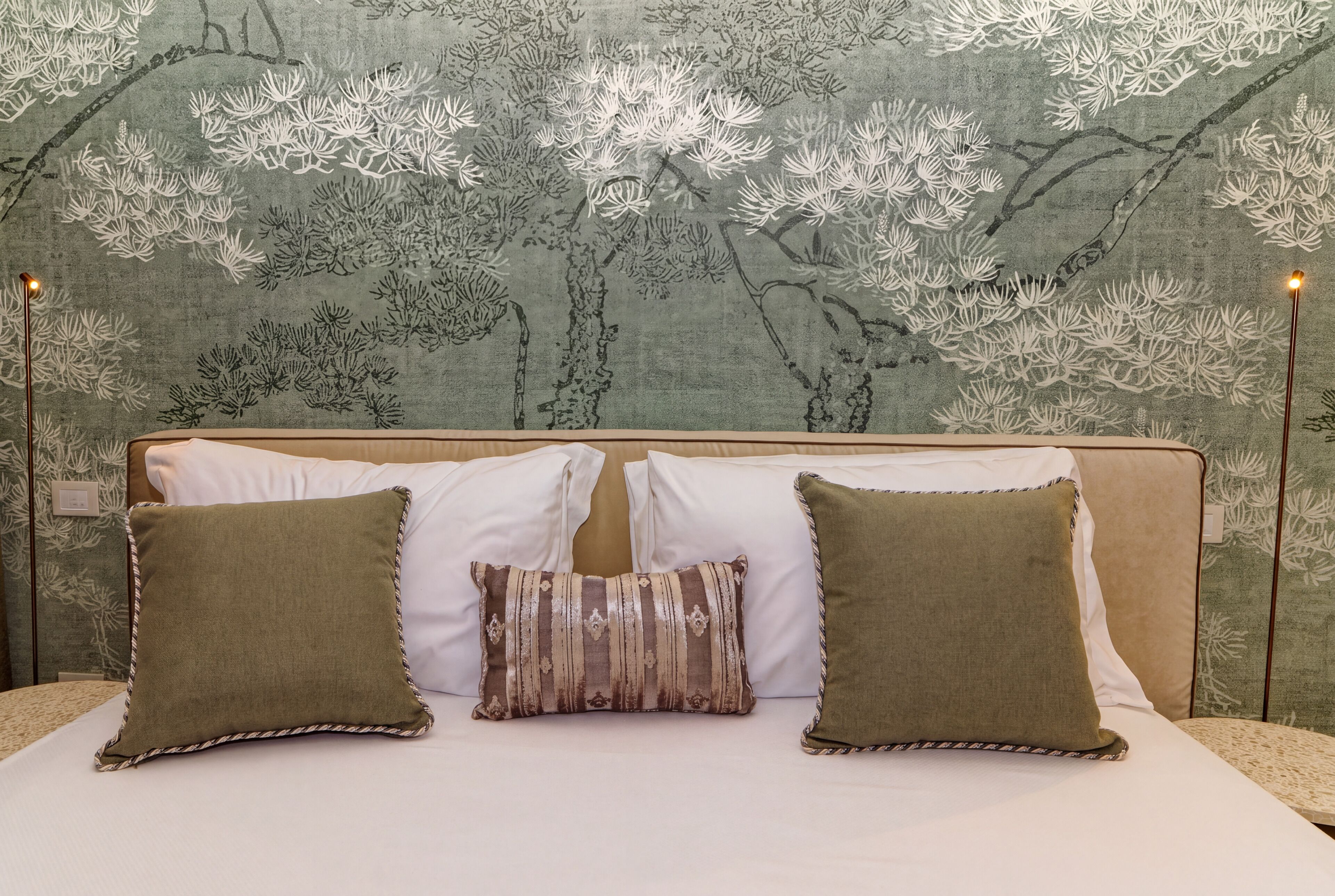 A bed with two pillows and a decorative headboard against a wall with a floral pattern.