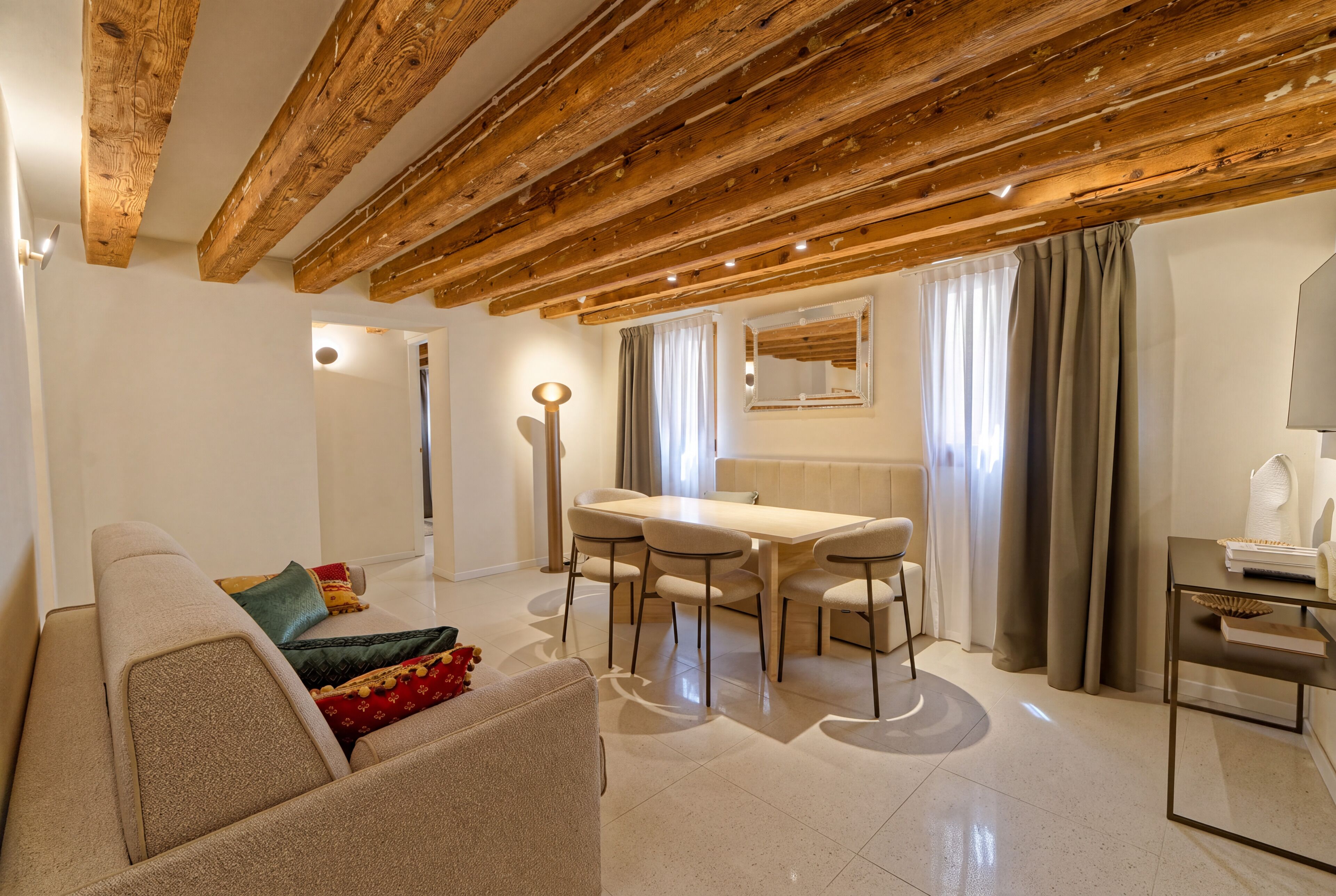 Un salon moderne avec un plafond en bois, un coin repas comprenant une table et des chaises, et un canapé agrémenté de coussins.