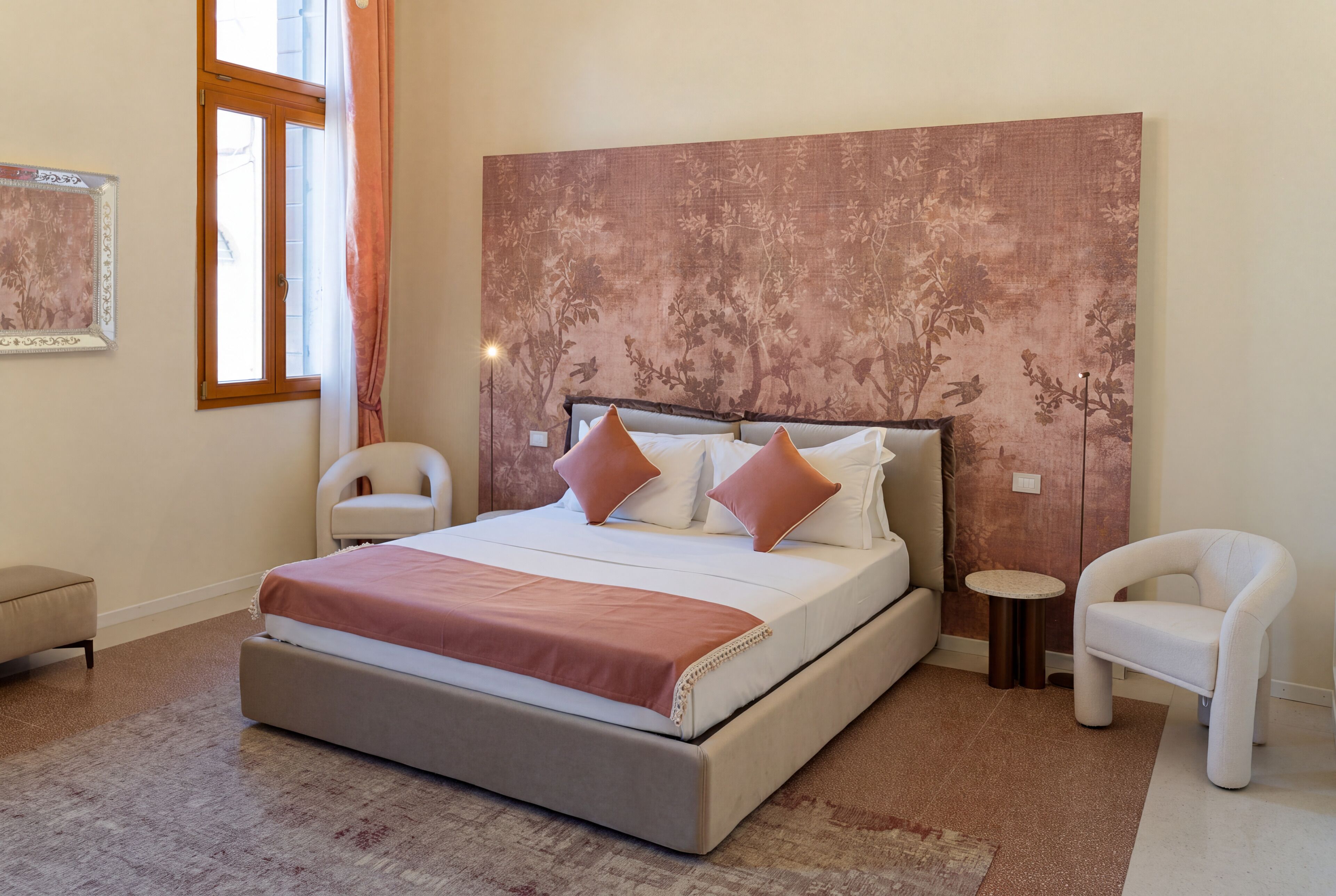 A bedroom with a large bed, two chairs, a small table, and a window.