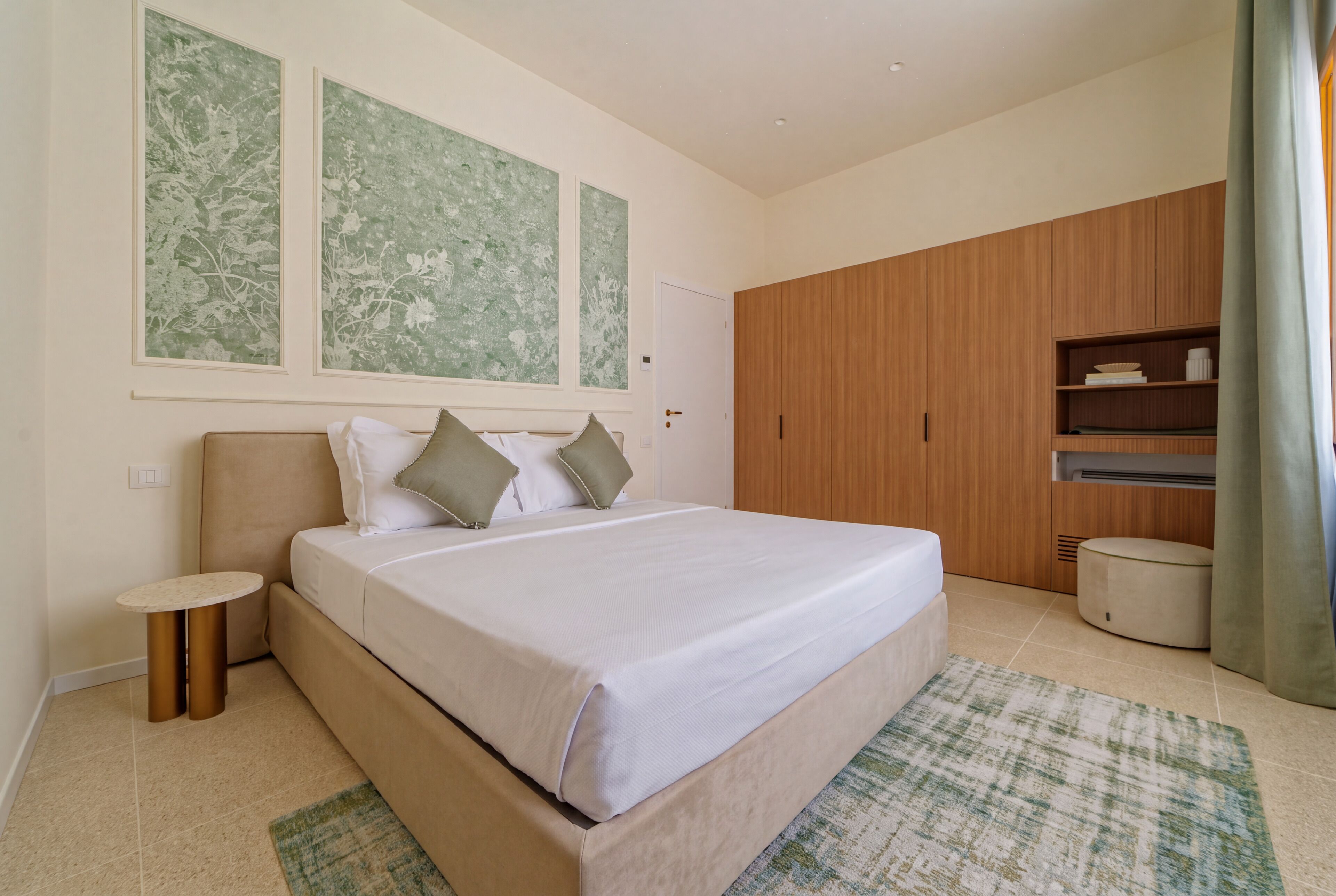 A modern bedroom with a large bed, a bedside table, a wardrobe, and a small round table.